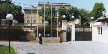 A formal consulate building with gates, flagpoles, and a uniformed guard
