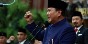 President Prabowo Subianto speaking at a podium with a raised fist