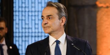 Greek Prime Minister Kyriakos Mitsotakis speaking at a podium, the named source behind the property transfer tax announcement
