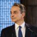 Greek Prime Minister Kyriakos Mitsotakis speaking at a podium, the named source behind the property transfer tax announcement
