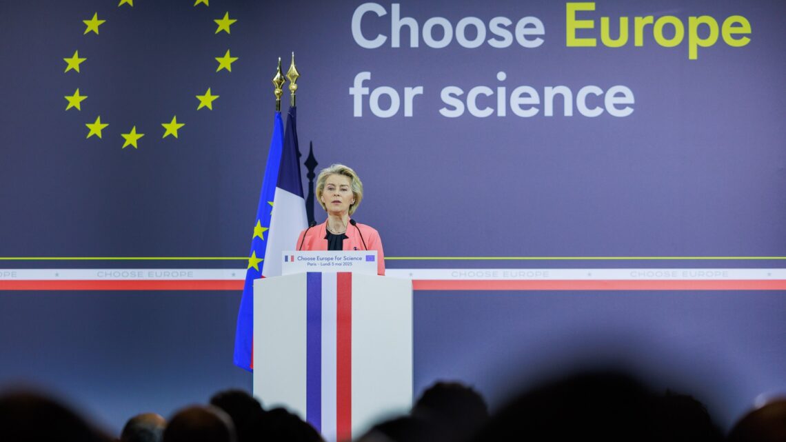 Ursula von der Leyen speaking at a podium with EU flag stars behind her