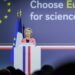 Ursula von der Leyen speaking at a podium with EU flag stars behind her