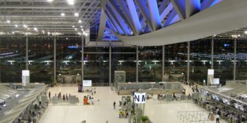Interior of Suvarnabhumi International Airport's main terminal hall in Bangkok, with check-in counters and travelers
