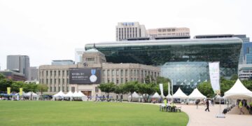 Seoul City Hall's distinctive glass-wave facade rising behind the old stone city hall building, with Seoul Plaza in front
