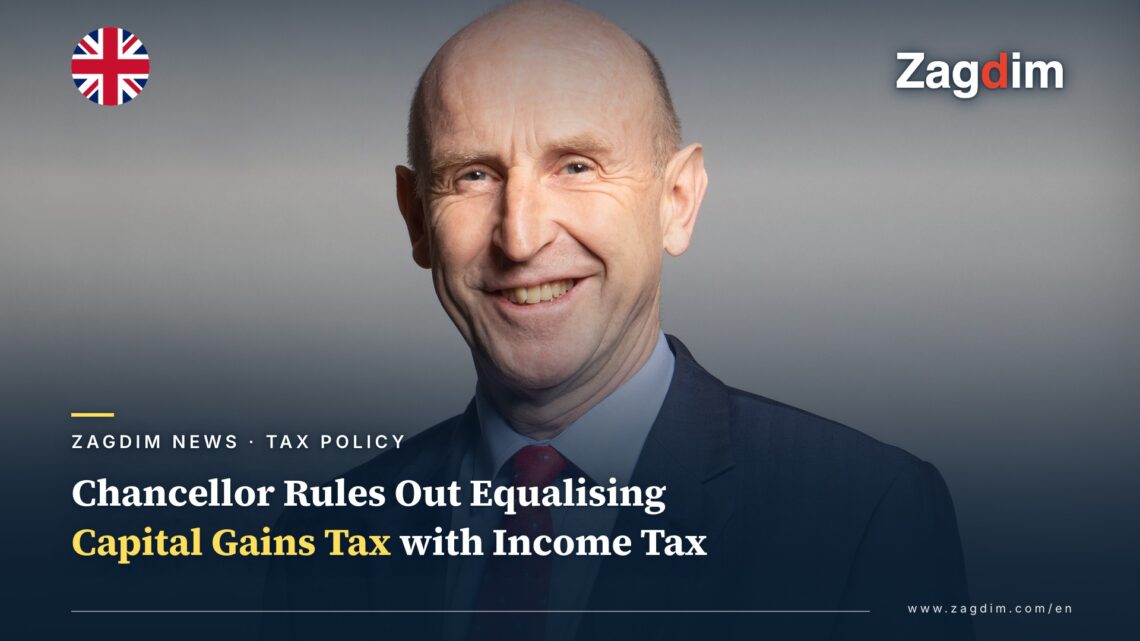 Official portrait of UK Chancellor John Healey, smiling against a grey backdrop, illustrating a story on his rejection of equalising capital gains tax with income tax