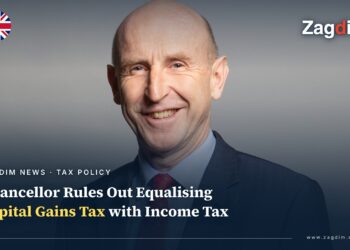 Official portrait of UK Chancellor John Healey, smiling against a grey backdrop, illustrating a story on his rejection of equalising capital gains tax with income tax