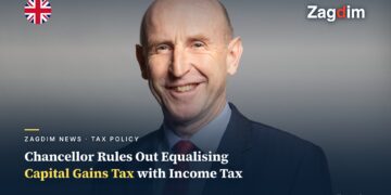 Official portrait of UK Chancellor John Healey, smiling against a grey backdrop, illustrating a story on his rejection of equalising capital gains tax with income tax