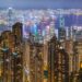 Dense residential apartment towers in the foreground with Victoria Harbour and Hong Kong's skyline behind, seen at night from Victoria Peak