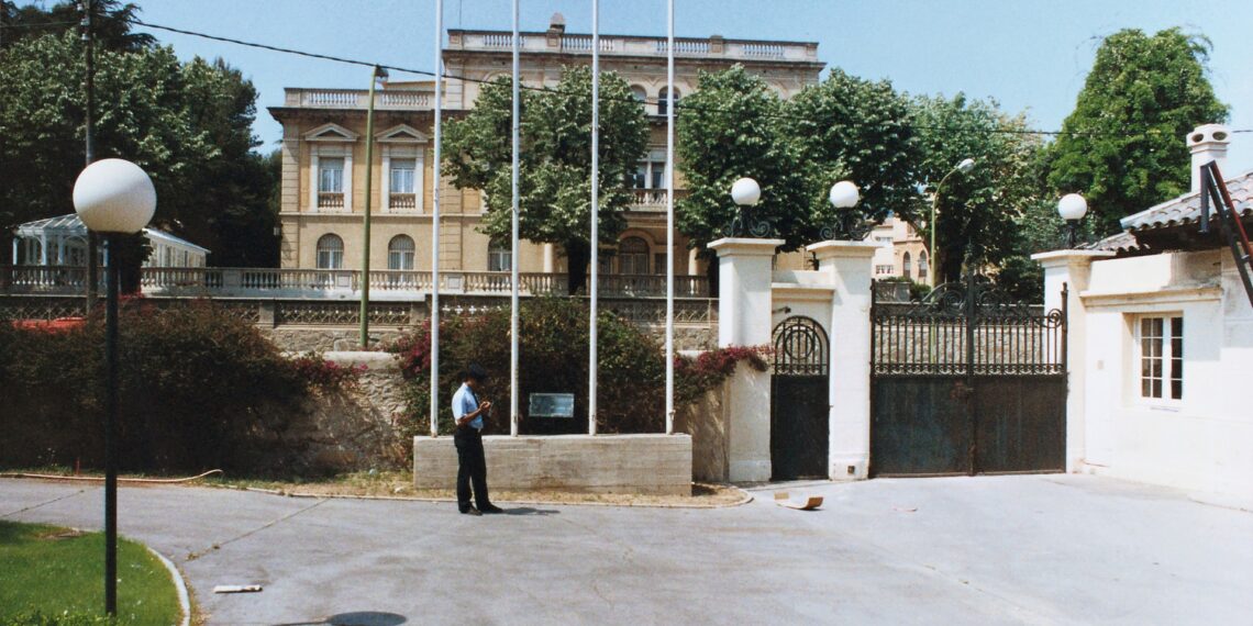 A formal consulate building with gates, flagpoles, and a uniformed guard