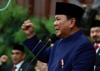 President Prabowo Subianto speaking at a podium with a raised fist