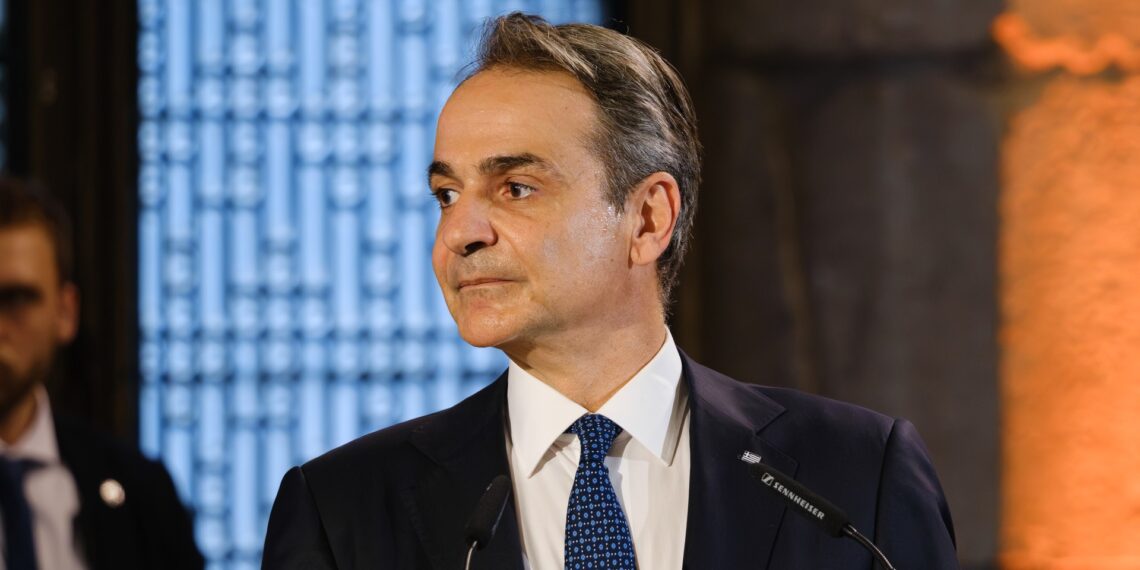 Greek Prime Minister Kyriakos Mitsotakis speaking at a podium, the named source behind the property transfer tax announcement