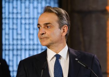 Greek Prime Minister Kyriakos Mitsotakis speaking at a podium, the named source behind the property transfer tax announcement
