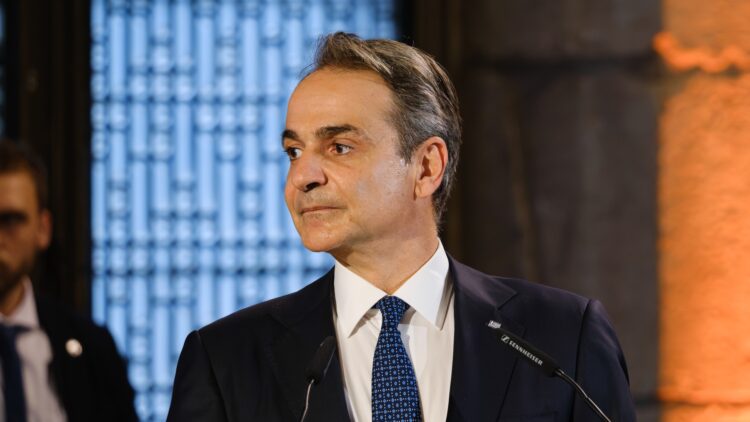 Greek Prime Minister Kyriakos Mitsotakis speaking at a podium, the named source behind the property transfer tax announcement