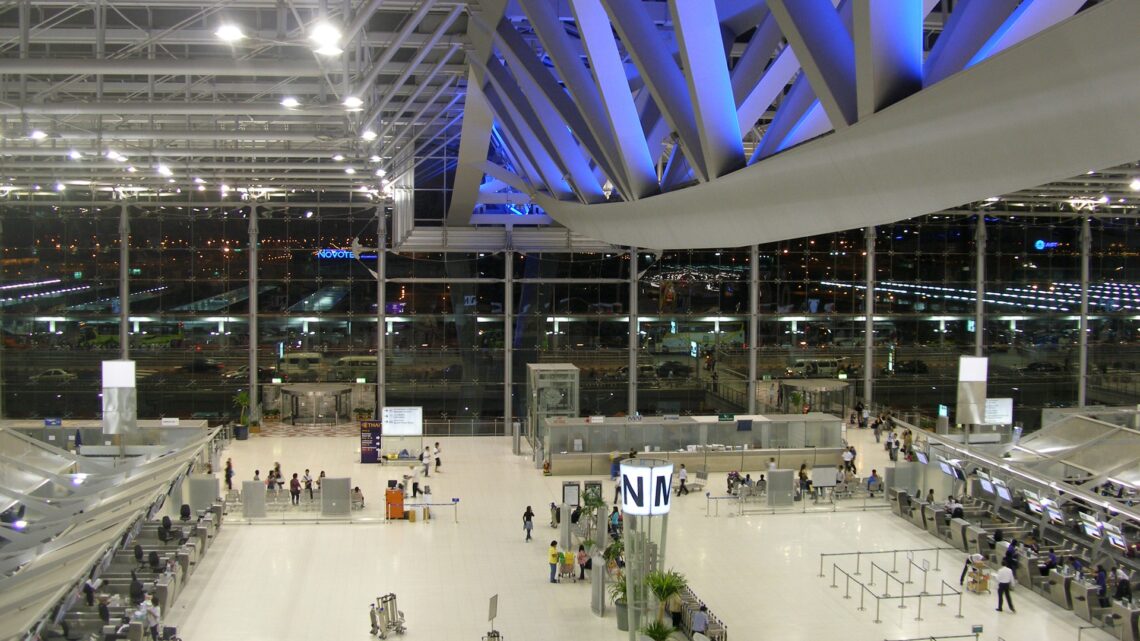 Interior of Suvarnabhumi International Airport's main terminal hall in Bangkok, with check-in counters and travelers