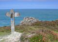A wooden waymarker sign on the Pembrokeshire Coast Path overlooking the sea and coastal rock outcrops
