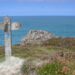 A wooden waymarker sign on the Pembrokeshire Coast Path overlooking the sea and coastal rock outcrops