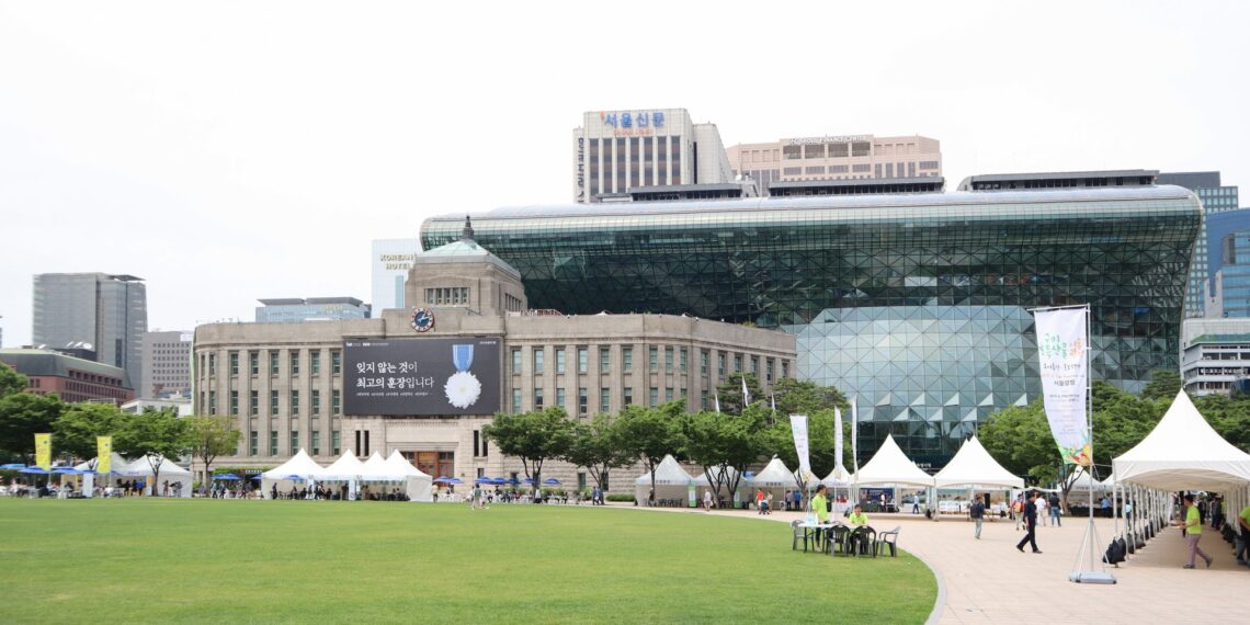 Seoul City Hall's distinctive glass-wave facade rising behind the old stone city hall building, with Seoul Plaza in front