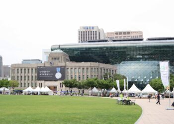 Seoul City Hall's distinctive glass-wave facade rising behind the old stone city hall building, with Seoul Plaza in front