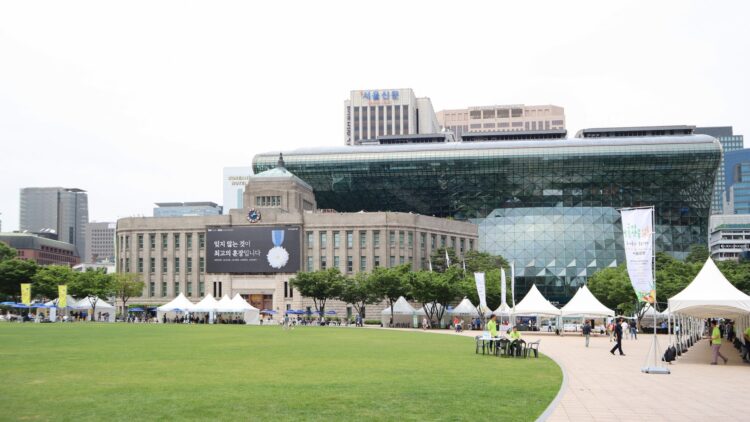 Seoul City Hall's distinctive glass-wave facade rising behind the old stone city hall building, with Seoul Plaza in front