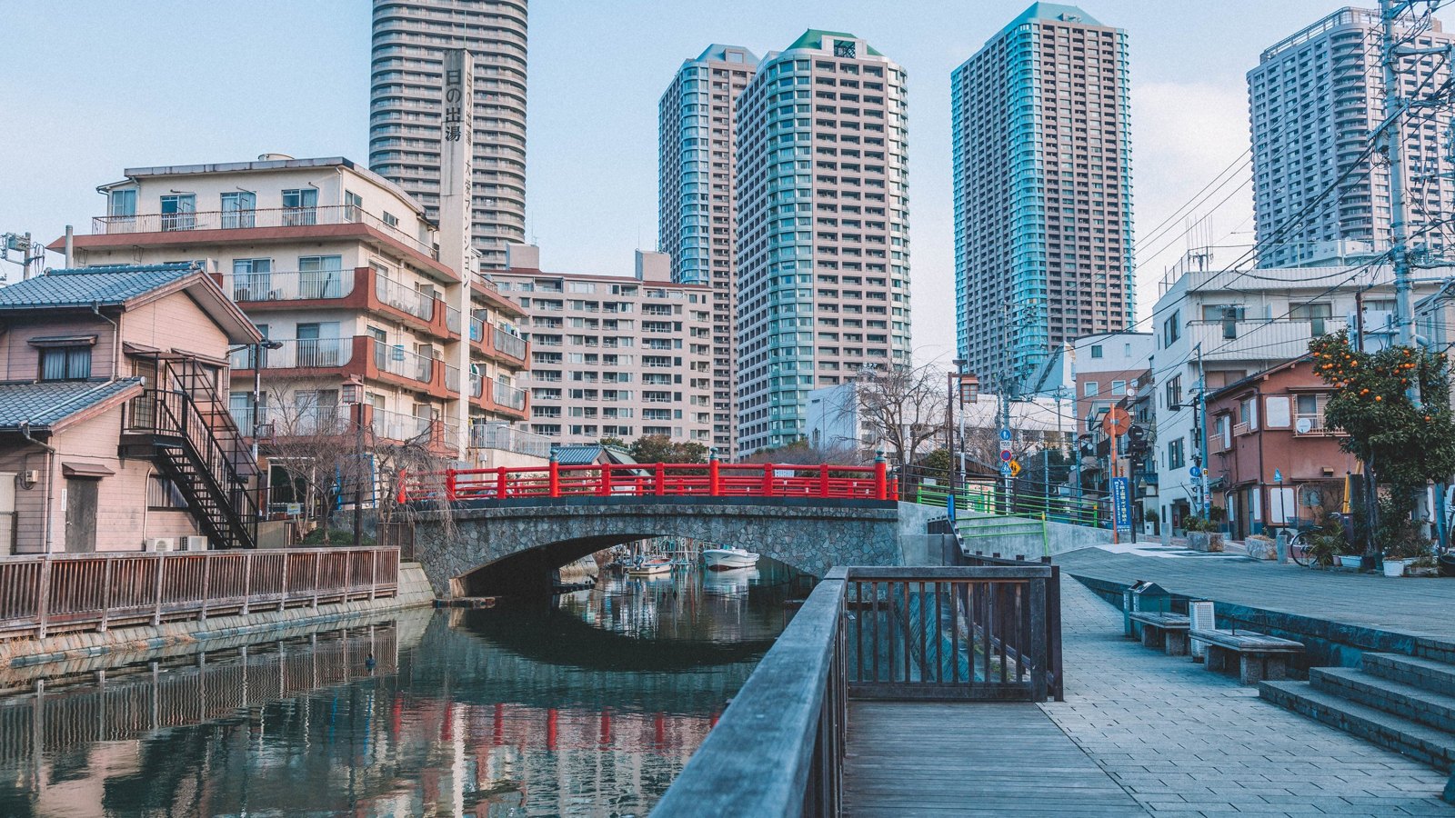 東京運河旁的石拱橋與紅色欄杆,後方是舊式公寓與高層公寓大樓