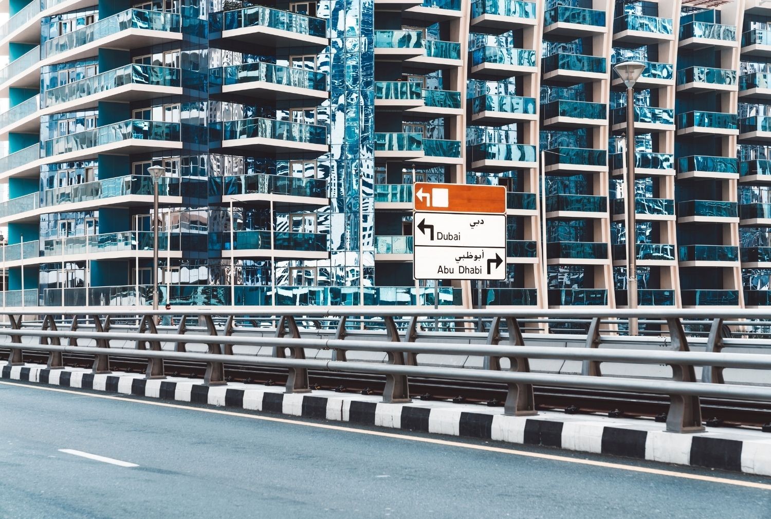 杜拜高架道路旁的指示牌,分別指向杜拜與阿布達比,背景是玻璃帷幕公寓大樓
