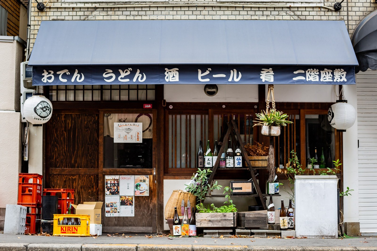 日本居酒屋店面,招牌寫著「酒」「ビール」,門口擺著一排日本酒酒瓶