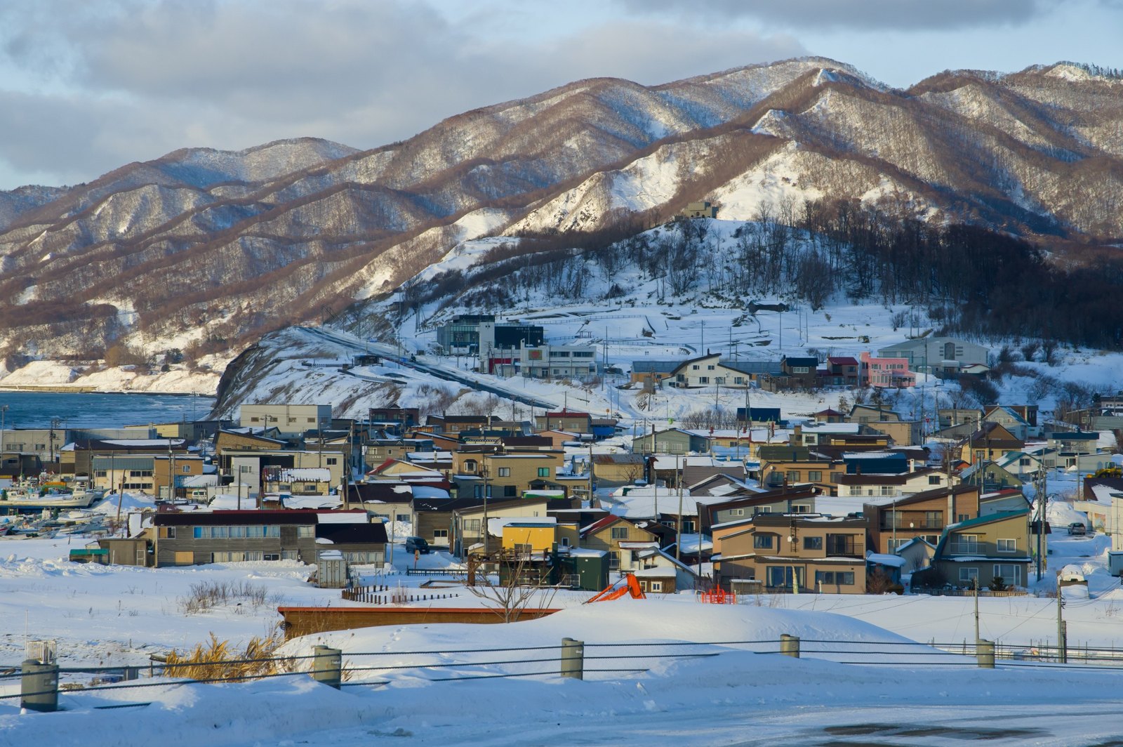 日本海岸小鎮的低層住宅被白雪覆蓋,背後是積雪的山
